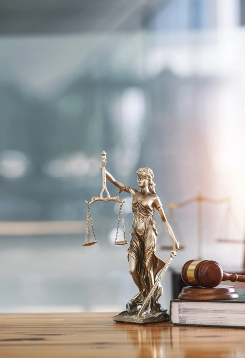 Statue der Richterdame mit Waagen der Gerechtigkeit und hölzernem Richterhammer auf Holztisch